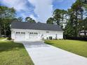 Three-car garage with white doors and long driveway surrounded by green grass and tall trees at 974 Crooked Oak Dr., Pawleys Island, SC 29585