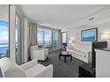 Bright living room with balcony access and ocean views features modern white furniture and gray carpeting at 107 S Ocean Blvd. # 1201, Myrtle Beach, SC 29577