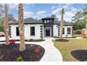 Striking home features a white exterior with black accents, landscaped yard, and inviting walkway to the front door at 1559 Old Tram Rd., Little River, SC 29566