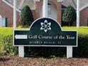 Sign for the Golf Course of the Year in Myrtle Beach, SC, set against a backdrop of brick buildings and greenery at 4482 Fringetree Dr., Murrells Inlet, SC 29576