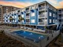 Coastal condo building at sunset, featuring a swimming pool and multiple levels with white balconies at 5600 Ocean Blvd. N # A11, North Myrtle Beach, SC 29582