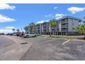 Seaside condo building with a gray facade, blue roof, and palm trees against a partly cloudy blue sky at 6001 N Ocean Blvd. # 147, North Myrtle Beach, SC 29582