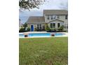 A view of a backyard pool, set amidst a lush green lawn and mature plantings, with a covered porch at 140 Zinnia Dr., Myrtle Beach, SC 29579