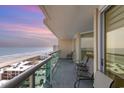 Oceanfront balcony with multiple chairs overlooks the beach and ocean waters against a colorful, pastel sky at 1707 Perrin Dr. # 1003, North Myrtle Beach, SC 29582