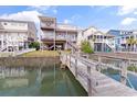 Rear view of three-story home featuring a private pier with dock in the backyard canal at 48 Sw Wilmington St., Ocean Isle Beach, NC 28469