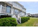 Townhouse exterior with white stairs and green shrubbery against a blue sky at 112 3Rd Ave. S # B, Surfside Beach, SC 29575