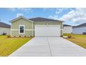 A view of a home with light green siding, showcasing a large two-car garage and manicured landscaping at 1372 Palm Springs Paloma Dr, Longs, SC 29568