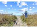 Sandy walkway leads to the beach and ocean under a blue sky with scattered clouds and tall grassy dunes at 3401 N Ocean Blvd. # 309, North Myrtle Beach, SC 29582