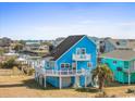 Beautiful blue two-story beach home featuring a wrap-around porch, ground-level entry, and lush landscaping in a coastal community at 154 Sand Dollar St., Holden Beach, NC 28462