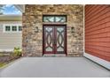Close-up of a stunning front door featuring glass panels and a stone exterior, illuminated by sconces at 3995 Tillmond Dr., Conway, SC 29526