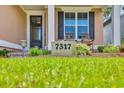 A close-up of the house number and charming front porch featuring two wooden chairs and lush landscaping at 7317 Lieth Ln., Sunset Beach, NC 28468