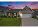 Charming single-story home with a well-manicured lawn, inviting front porch, and attached two-car garage at sunset at 505 Joy Way Ct., Longs, SC 29568