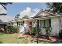 Charming single-story home with a metal roof, white painted brick, black shutters, manicured bushes, and a red front door at 1014 Bay Dr., Surfside Beach, SC 29575