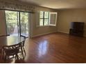 Living room with hardwood floors, large window with shutter, sliding glass door to a balcony, and a wooden dining table at 5001 Little River Rd. # W-211, Myrtle Beach, SC 29577