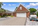 Brick house featuring a two-car garage and paved driveway complemented by well-manicured landscaping and lush green trees at 702 Compass Pointe Dr, North Myrtle Beach, SC 29582