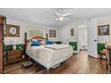 Well-lit bedroom featuring hardwood floors, a ceiling fan, a bed with green trim and an open bathroom door at 3839 Woodridge Circle, Little River, SC 29566