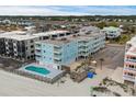 Aerial view of light blue three-story condo building, neighborhood, outdoor pool, and beach at 824 N Waccamaw Dr. # 203, Murrells Inlet, SC 29576