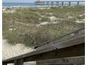 A scenic view of a sandy beach with a pier in the distance, viewed from the top of wooden stairs at 1432 Seahouse Ct., Surfside Beach, SC 29575