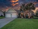 Twilight view of charming one-story home with a two-car garage, manicured lawn, and palm trees at 1635 Southwood Dr., Surfside Beach, SC 29575