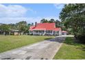 Beautiful home showcasing a red metal roof, long driveway, and lush green lawn, surrounded by mature trees at 1700 Longleaf Dr., Myrtle Beach, SC 29575