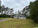View of the front of the house with an attached carport and surrounding yard with mature trees at 321 Circle Heights Dr., Loris, SC 29569