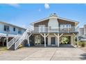 Exterior view of elevated beach home with white railings, gray stairs and brick facade at 204 55Th Ave. N, North Myrtle Beach, SC 29582