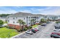 View of the condo complex with well-maintained landscaping and palm trees and ample parking at 4142 Hibiscus Dr. # 102, Little River, SC 29566