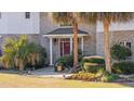 Home's entrance with brickwork, pillars, red door, and a neatly landscaped yard with palms at 4552 River Rd., Little River, SC 29566