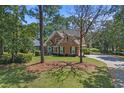 A brick home is surrounded by mature trees, a well-manicured lawn, and a colorful front door and black shutters at 3975 River Hills Dr., Little River, SC 29566