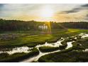 A beautiful home is set in a lush landscape, with a golden sun setting behind it and reflecting off a nearby river at 288 Tipperary Pl., Pawleys Island, SC 29585