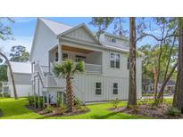 Beautifully landscaped, a two-story home featuring a metal roof and a welcoming staircase at 205 Jackrabbit Place, Pawleys Island, SC 29585