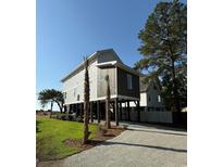 Coastal home featuring a raised foundation, driveway, and lush lawn with palm trees in a sunny neighborhood at 189 Brown Pelican Loop, Pawleys Island, SC 29585