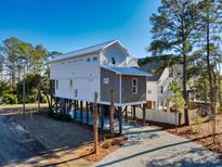 Coastal home on stilts featuring a light gray exterior, metal roof, and a paved driveway at 189 Brown Pelican Loop, Pawleys Island, SC 29585