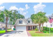 Charming two-story home featuring lush landscaping, palm trees, and an attached two-car garage at 627 3Rd Ave. S, Surfside Beach, SC 29575