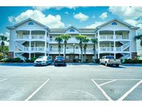 Three-story condo building with white balconies, stairs, and palm trees in front of the parking lot at 5801 Oyster Catcher Dr. # 434, North Myrtle Beach, SC 29582