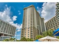 View of the tall condo building with many windows, balconies, and lush tropical landscaping at 9994 Beach Club Dr. # 205, Myrtle Beach, SC 29572