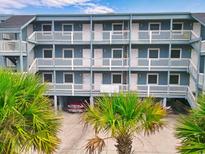 Coastal condo building showcasing multiple levels with white railings, balconies, and a covered parking area with a red car at 116 S Waccamaw Dr. # 104, Garden City Beach, SC 29576