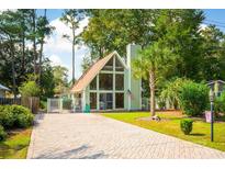 A-frame home with large windows, a brick driveway, palm tree, and well-manicured lawn creates a welcoming exterior at 617 3Rd Ave. S, Surfside Beach, SC 29575