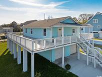 Elevated home with light blue exterior, spacious deck, and attached garage at 243 Calhoun Dr., Garden City Beach, SC 29576