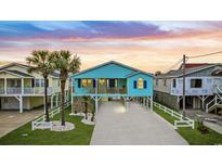 Charming beach house with a raised foundation, palm trees, and a white picket fence at sunset at 6205 Nixon St., North Myrtle Beach, SC 29582