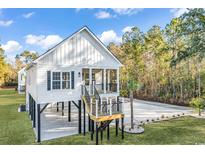 Charming elevated beach house featuring a white exterior, black accents, and a well-manicured lawn at 33 Captains Pl, Murrells Inlet, SC 29576