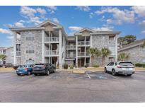 Three-story condo with stone facade, white railings, and ample parking on a sunny day at 4761 Wild Iris Dr. # 103, Myrtle Beach, SC 29577