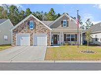 Charming home featuring a stone facade, two-car garage, and inviting front porch with an American flag at 528 Fanciful Way, Myrtle Beach, SC 29588