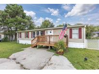 Mobile home with front deck, American flag, and landscaped yard at 3845 Woodridge Circle, Little River, SC 29566