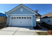 A well-lit, pale blue house with a white garage door featuring decorative windows and black hardware at 1253 Lady Bird Way, North Myrtle Beach, SC 29582