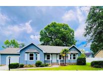 Charming blue home with white trim, a well-manicured lawn, and mature trees under a partly cloudy sky at 104 Willow Ridge Rd., Myrtle Beach, SC 29588