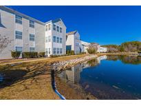 Scenic view of gray condo buildings by a calm lake under a clear blue sky, nestled within a well-maintained community at 2268 Essex Dr. # L, Surfside Beach, SC 29575