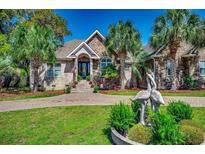 Beautiful brick home featuring mature palm trees, a circular driveway, and a charming crane statue in a lovely landscaped yard at 2803 Ships Wheel Dr., North Myrtle Beach, SC 29582