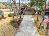 Brick home featuring a two-car garage, long driveway, and mature trees in a lakeside community at 3178 River Bluff Ln., Little River, SC 29566