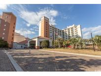 Beautiful condo building exterior with brick entrance, tower, and manicured grounds on a partly cloudy day at 8121 Amalfi Pl. # 4-702, Myrtle Beach, SC 29572